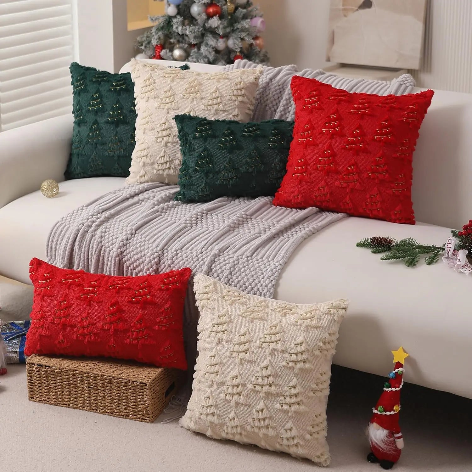 Coussins décoratifs aux motifs de sapins, rouge, vert et crème, sur un canapé blanc avec un plaid gris