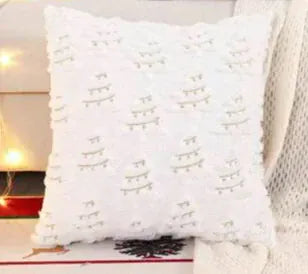 Coussin décoratif blanc avec motifs de sapins, posé sur un canapé, ajoutant une touche festive à la décoration