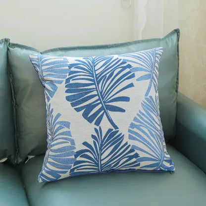Coussin décoratif avec motifs de feuilles tropicales bleues sur fond clair, posé sur un canapé vert