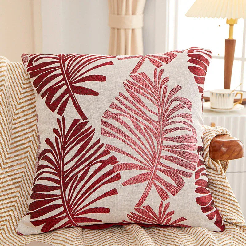 Coussin décoratif avec motifs de feuilles rouges sur fond beige, posé sur un canapé au style chaleureux