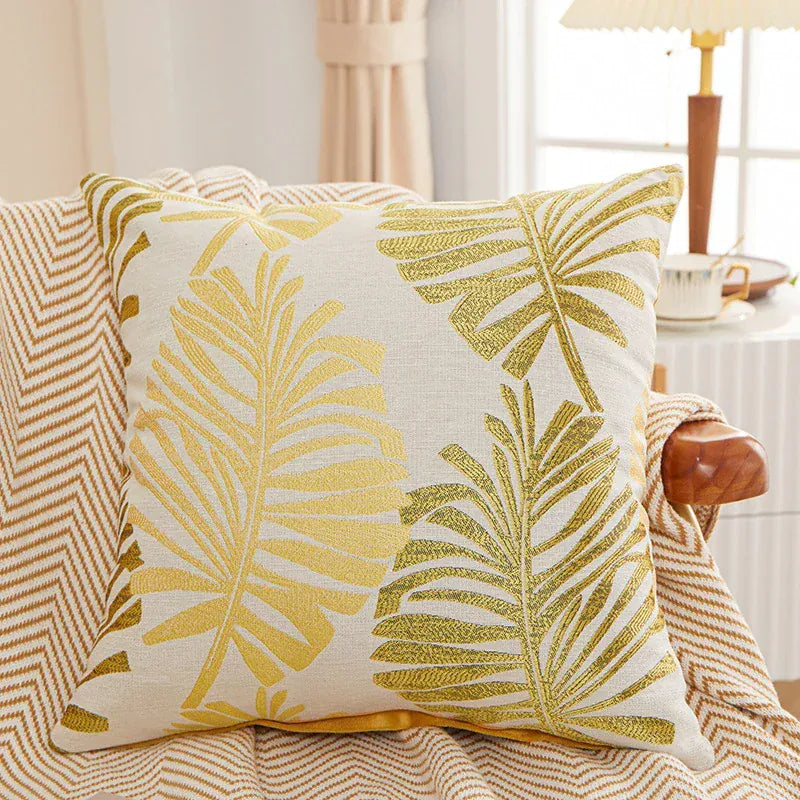 Coussin décoratif avec motifs de feuilles tropicales jaunes sur fond crème, posé sur un canapé à rayures