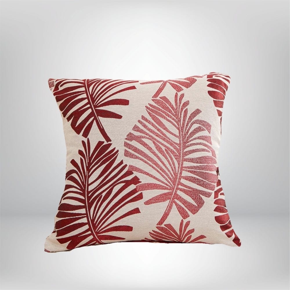 Coussin décoratif avec un motif tropical de feuilles rouges sur fond beige, idéal pour un canapé ou un lit