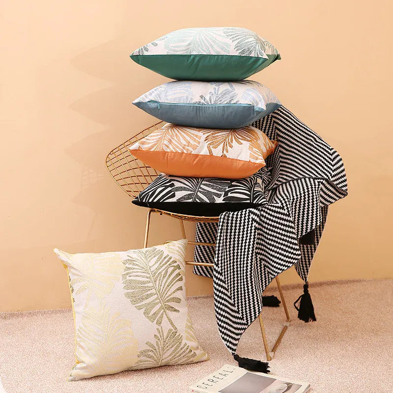 Housses de coussin décoratives aux motifs tropicaux, empilées sur une chaise dorée, avec un plaid noir et blanc