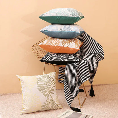 Housses de coussin décoratives aux motifs tropicaux, empilées sur une chaise dorée, avec un plaid noir et blanc