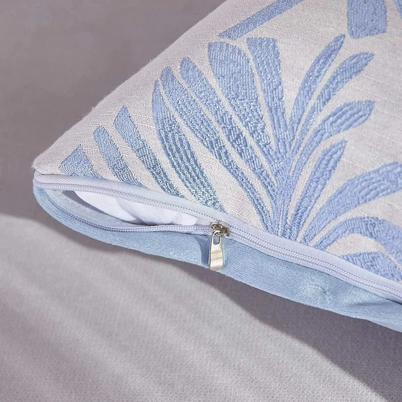 Housse de coussin décorative avec motifs de feuilles bleues sur fond clair, posée sur un canapé
