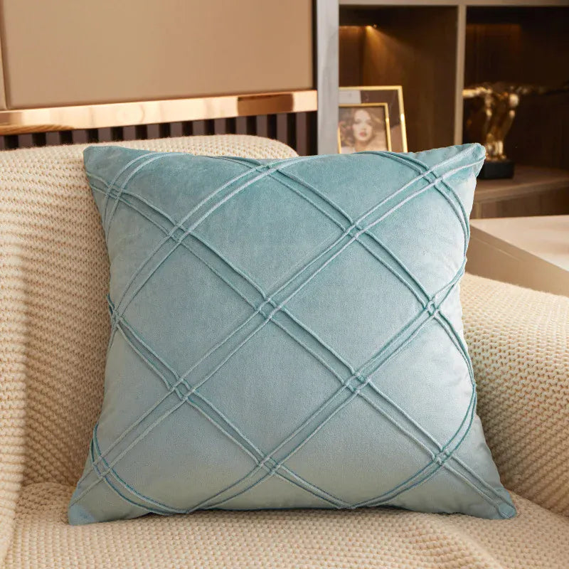 Coussin déco en velours bleu clair avec motif en losanges, posé sur un canapé beige texturé