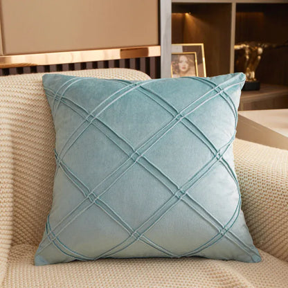 Coussin déco en velours bleu clair avec motif en losanges, posé sur un canapé beige texturé