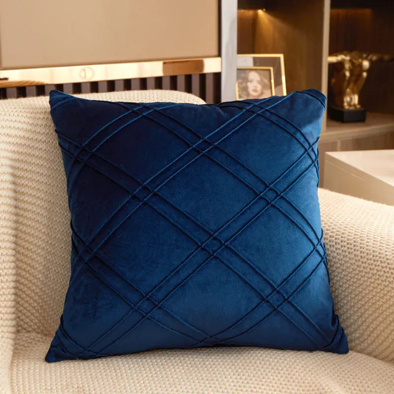 Coussin déco en velours bleu marine avec motifs en losanges, posé sur un canapé beige texturé