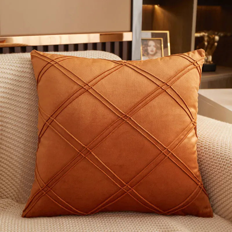 Coussin décoratif en velours orange avec motifs en losanges, posé sur un canapé beige dans un salon moderne