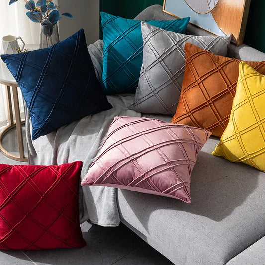 Coussins décoratifs en velours aux couleurs variées, disposés sur un canapé gris, avec motifs en relief