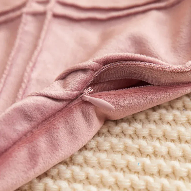 Housse de coussin en velours rose avec fermeture éclair, posée sur un tissu tricoté beige