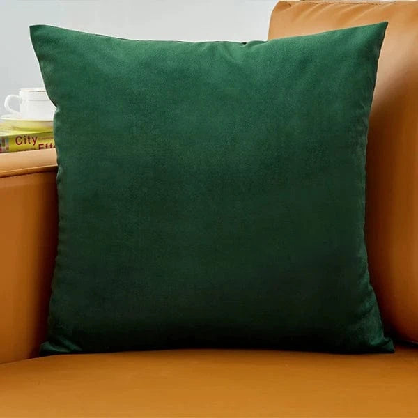 Coussin déco en velours vert posé sur un canapé en cuir marron, ajoutant une touche d'élégance à la pièce