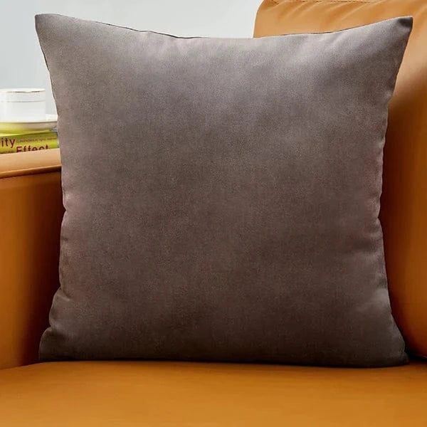 Coussin décoratif en velours gris posé sur un canapé en cuir orange, apportant élégance et douceur à la décoration