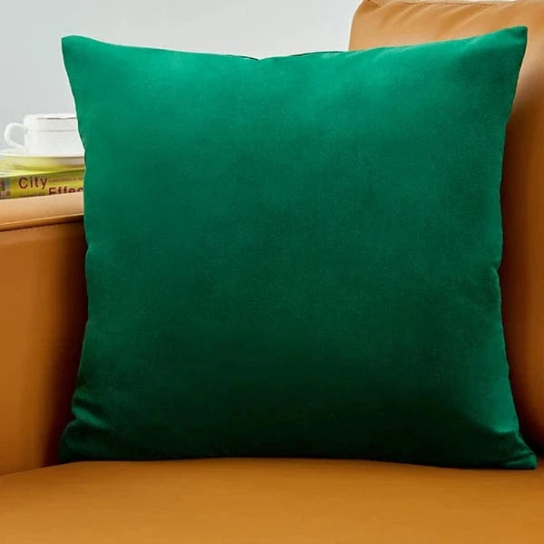 Coussin déco en velours vert profond posé sur un canapé marron, ajoutant une touche d'élégance et de confort
