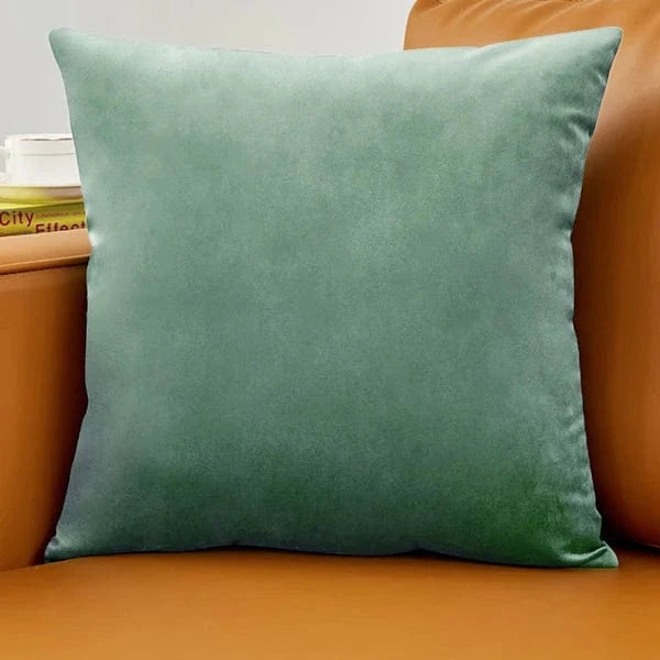 Coussin déco en velours vert posé sur un canapé en cuir marron, ajoutant une touche d'élégance à la décoration
