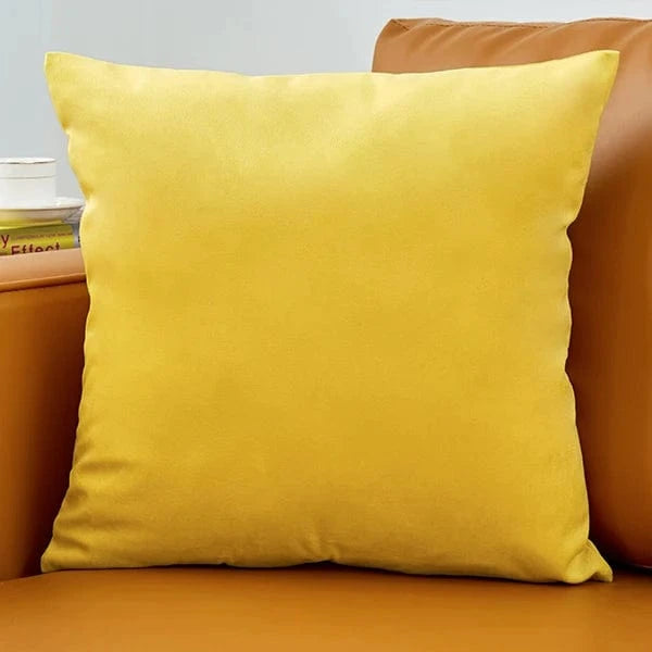 Coussin déco en velours jaune, posé sur un canapé en cuir marron, apportant élégance et douceur à la décoration