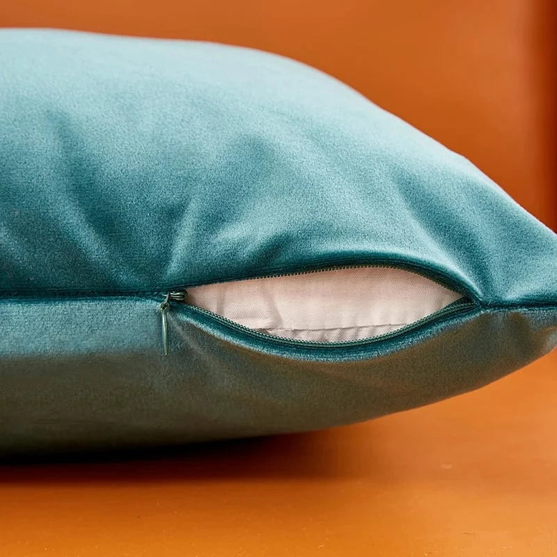 Housse de coussin en velours turquoise avec fermeture éclair, posée sur un fond orange, ajoutant une touche chic à la