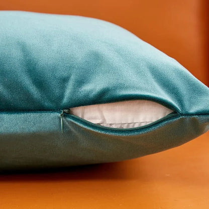 Housse de coussin en velours turquoise avec fermeture éclair, posée sur un fond orange, ajoutant une touche chic à la
