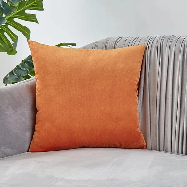Coussin déco en velours orange posé sur un canapé gris, ajoutant une touche d'élégance à la pièce