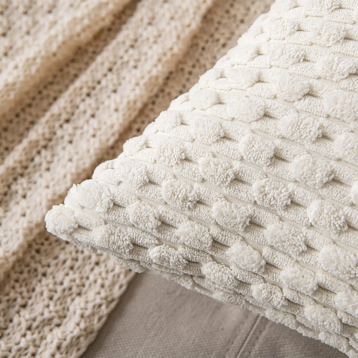 Coussin décoratif en tissu beige texturé, avec des motifs en relief, posé sur un canapé neutre