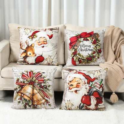 Quatre coussins décoratifs aux motifs de Noël sur un canapé beige, représentant le Père Noël et des cloches dorées