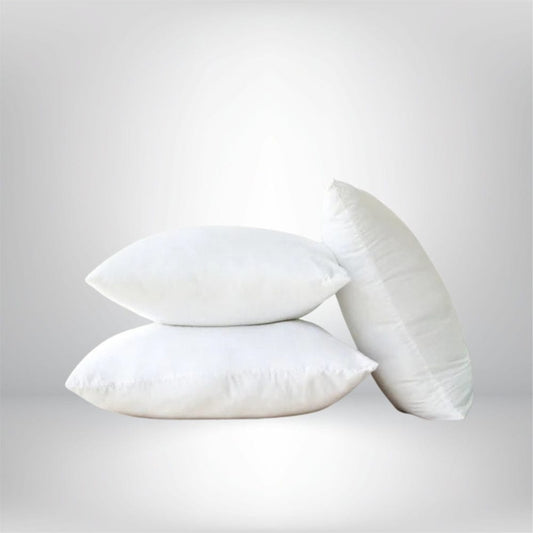 Trois coussins décoratifs blancs en forme rectangulaire et ronde, posés sur un fond neutre